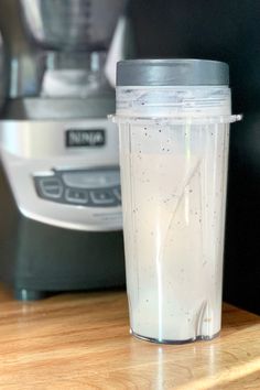 a blender sitting on top of a wooden counter next to a cup filled with liquid