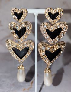 These stunning heart-shaped earrings feature three delicate hearts, gracefully dangling from a captivating gold outer interior with rhinestones for that extra sparkle. Adorn yourself with timeless beauty and express your love with every sway. Elegant Black Heart Earrings For Anniversary, Metal Earrings With Heart Charm For Party, Elegant Metal Heart Earrings For Valentine's Day, Glamorous Double Heart Jewelry For Parties, Double Heart Rhinestone Jewelry For Party, Elegant Double Heart Metal Earrings, Chic Heart Charm Jewelry For Party, Black Double Heart Jewelry For Party, Elegant Double Heart Rhinestone Jewelry