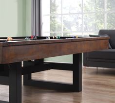 a pool table with balls on it in front of a couch and chair near a window