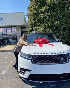 a man standing next to a white range rover with a red bow on it's hood