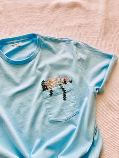 This hand embroidered wildflower t-shirt is a perfect simple capsule piece that can be paired easily! Unisex sizing and preshrunk cotton material, so comfortable and easy to wear. CARE: -Turn inside out, and wash cold on delicate -Tumble dry on low, or hang dry -Turn inside out to iron Each t-shirt is hand embroidered and by nature may vary slightly from the image shown. Each embroidered piece is my own original design. This piece cannot be customized. If you would like a customized t-shirt, ple Embroidery Shirt Pocket, Tshirt Pocket Embroidery, Pocket Tee Embroidery, Blue Shirt Embroidery, Embroidered Pocket Tees, Embroided T Shirts, Shirt Pocket Embroidery, Embroidered Shirt Ideas, Embroidered Clothes Diy