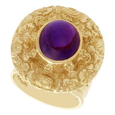 An impressive vintage 3.77 carat amethyst and 9 karat yellow gold cocktail ring; part of our diverse amethyst jewelry and estate jewelry collections. This fine and impressive vintage amethyst ring has been crafted in 9k yellow gold. The ring has an oval form, embellished with a textured floral design. The center of the floriated design is ornamented with a feature 3.77Ct oval cabochon cut amethyst, bezel set in relief. The multi-stranded, pierced decorated and shaped ring shoulders integrate wit Luxury Round Cabochon Amethyst Ring, Formal Cabochon Amethyst Ring Fine Jewelry, Fine Jewelry Purple Amethyst Cabochon Ring, Purple Amethyst Cabochon Ring Fine Jewelry, Yellow Gold Amethyst Cabochon Ring, Heirloom Cabochon Amethyst Ring For Anniversary, Luxury Collectible Amethyst Ring, Cabochon Amethyst Ring In Fine Jewelry Style, Yellow Gold Amethyst Ring With Polished Finish