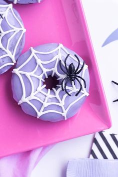 two donuts decorated with white icing and spider webs on a pink plate