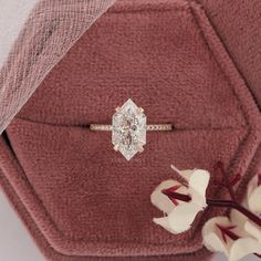 an engagement ring sitting on top of a red velvet bag with flowers in front of it