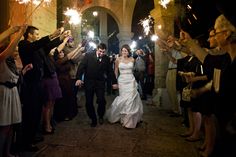 a bride and groom walk through the crowd with their sparklers