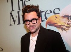 a man wearing glasses standing in front of a wall with an eagle on it's face