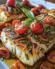 some fish with tomatoes and herbs on top of it in a dish that is ready to be eaten