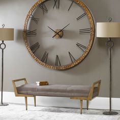 a large clock mounted to the side of a wall next to a bench and lamp