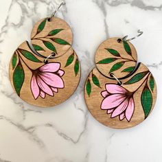 two wooden earrings with pink flowers painted on them sitting on a marble countertop next to each other