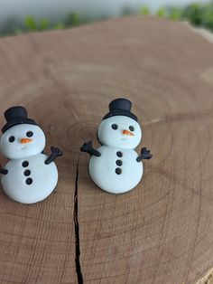 two small snowmen sitting on top of a piece of wood