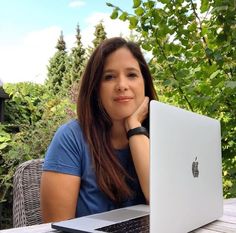 a woman sitting in front of a laptop computer on top of a wooden table next to a tree