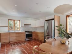 a kitchen with tile flooring and wooden cabinets in the center, surrounded by windows