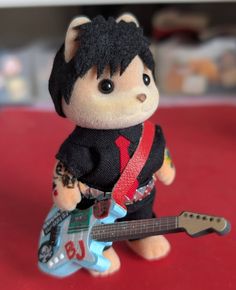 a small stuffed animal with a guitar in it's hand on a red surface