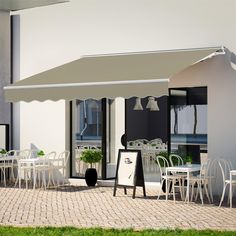 an outdoor dining area with white chairs and tables under a large awning on the side of a building