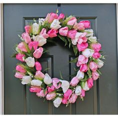 a wreath with pink and white tulips is hanging on the front door,