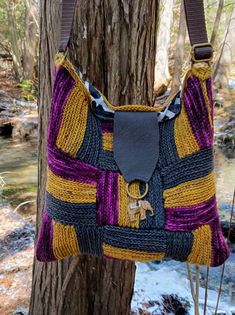 a handbag hanging from a tree in the woods with water behind it and snow on the ground