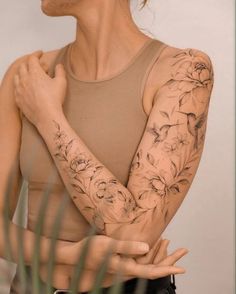 a woman with tattoos on her arms and arm is standing in front of a plant