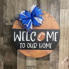 a wooden sign that says welcome to our home with a football and blue bow on it