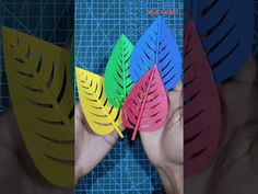 four different colored leaves are being held by someone's hands in front of a blue background