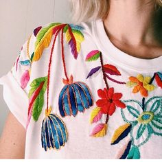 a woman with blonde hair wearing a white t - shirt with colorful flowers on it