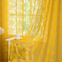 a window with yellow lace curtains and a white vase sitting on a table in front of it