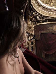 a woman sitting in front of a red velvet covered chair with her back turned to the camera