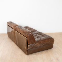 a brown leather couch sitting on top of a wooden floor next to a white wall