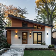 This stylish Scandinavian bungalow features a striking sloped roof and a blend of white stucco and wood siding. Large windows and a sleek door, flanked by minimalist wall lights, enhance the modern facade. The front yard boasts a paved walkway and a lush lawn, complementing the clean lines and natural materials. This design beautifully merges traditional Scandinavian elements with contemporary architecture, making it a perfect blend of elegance and modernity. One Side Roof House Design, Stucco Two Story House, White House With Wood Posts, Country Home Designs Exterior, House Design Wood Modern, Houses Exterior Simple, Skillion Roof Facade Modern Exterior, Scandinavian Exterior Design Small House, Bungalow Lake House