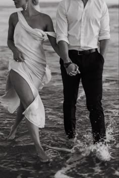 a man and woman are walking in the water holding each other's hands as they walk into the ocean