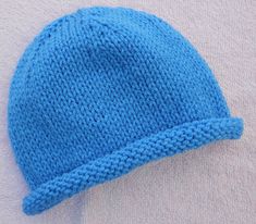 a blue knitted hat laying on top of a white blanket next to a wall