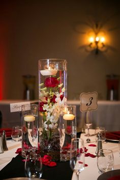 a centerpiece with candles and flowers is displayed on a table in front of wine glasses