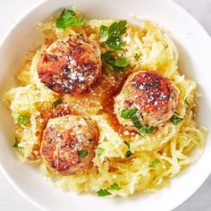 a white bowl filled with spaghetti and meatballs covered in parmesan cheese sauce