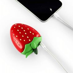 a red strawberry shaped device plugged into a charger next to a cell phone