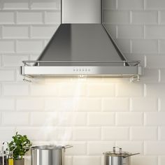 a stainless steel range hood over two pots and pans