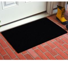 a black door mat sitting on top of a red brick floor next to a pair of yellow boots