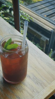 a drink sitting on top of a wooden table next to a green leafy plant