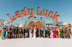 Celebrate love under the dazzling "Lady Luck" neon sign in this delightful outdoor wedding! The bride stuns in a timeless wedding dress, while guests flaunt colorful fall wedding guest dresses. The vintage ambiance and cheerful crowd capture the essence of epic wedding ideas, perfect for those hunting unique, retro-themed inspirations 🌟💐✨. #WeddingIdeas #Wedding #FallWedding #BackyardWedding #UniqueWeddingIdeas Colorful Fall Wedding, Fall Wedding Guest Dresses, Retro Romance, Epic Wedding, Lady Luck