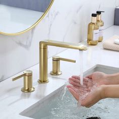 a person washing their hands under a faucet in a bathroom with gold fixtures