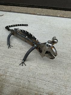 a metal lizard sitting on top of a cement floor next to a door way with it's tail curled up