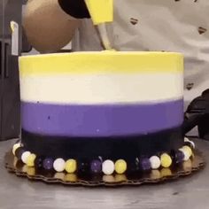 a person is decorating a cake with yellow and purple frosting