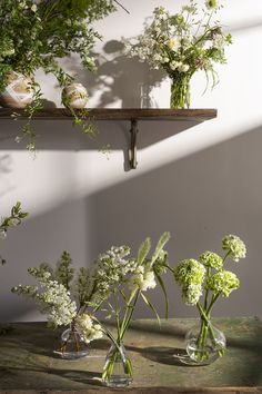 three vases filled with flowers sitting on top of a wooden table next to a wall