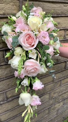 a bridal bouquet hanging on the side of a brick wall in front of a woman's hand