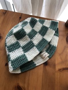 two green and white crocheted hats sitting on top of a wooden table next to a window