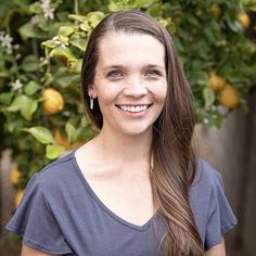 a woman with long brown hair smiling at the camera in front of some lemon trees