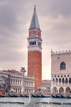 a tall clock tower towering over a city next to water with boats in the foreground