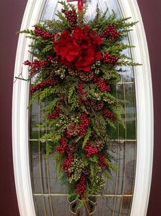 a wreath is hanging on the front door with red berries and greenery in it