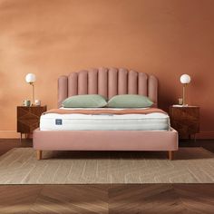 a bed with pink upholstered headboard against an orange wall