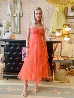 a woman in an orange dress standing next to a black chair and wall with pictures on it