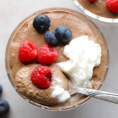 two desserts with berries, cream and blueberries in them on a white table