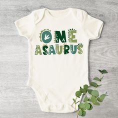 a baby bodysuit with the words one asaurs printed on it next to a plant